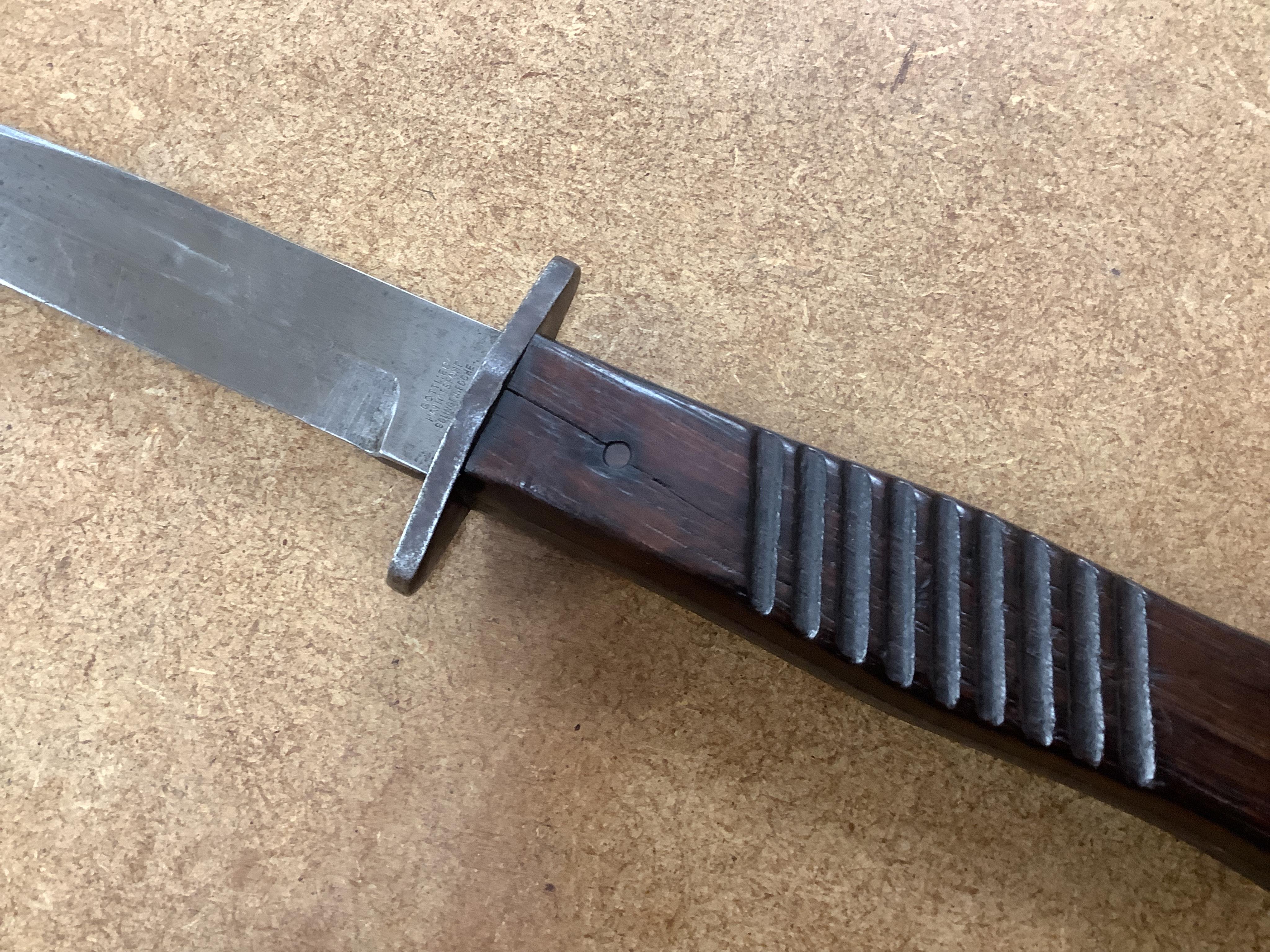 A First World War German Fighting Knife, with two piece wooden grip and steel cross guard, in original steel scabbard with leather belt loop mount, single edged blade with makers mark to one side; Gottlieb Hammesfahr, So